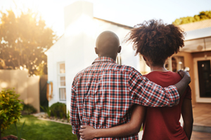 A couple, standing arm-in-arm, looking at the exterior of their home.